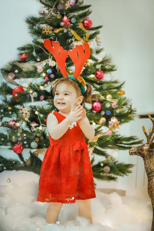 Free Cute child in festive outfit with antlers at Christmas tree, smiling. Stock Photo