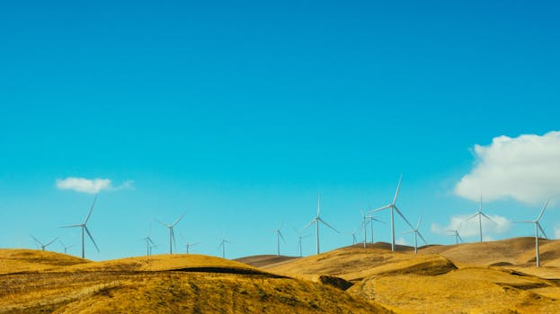 Wind turbines on a sunny day generate clean energy on rolling golden hills.