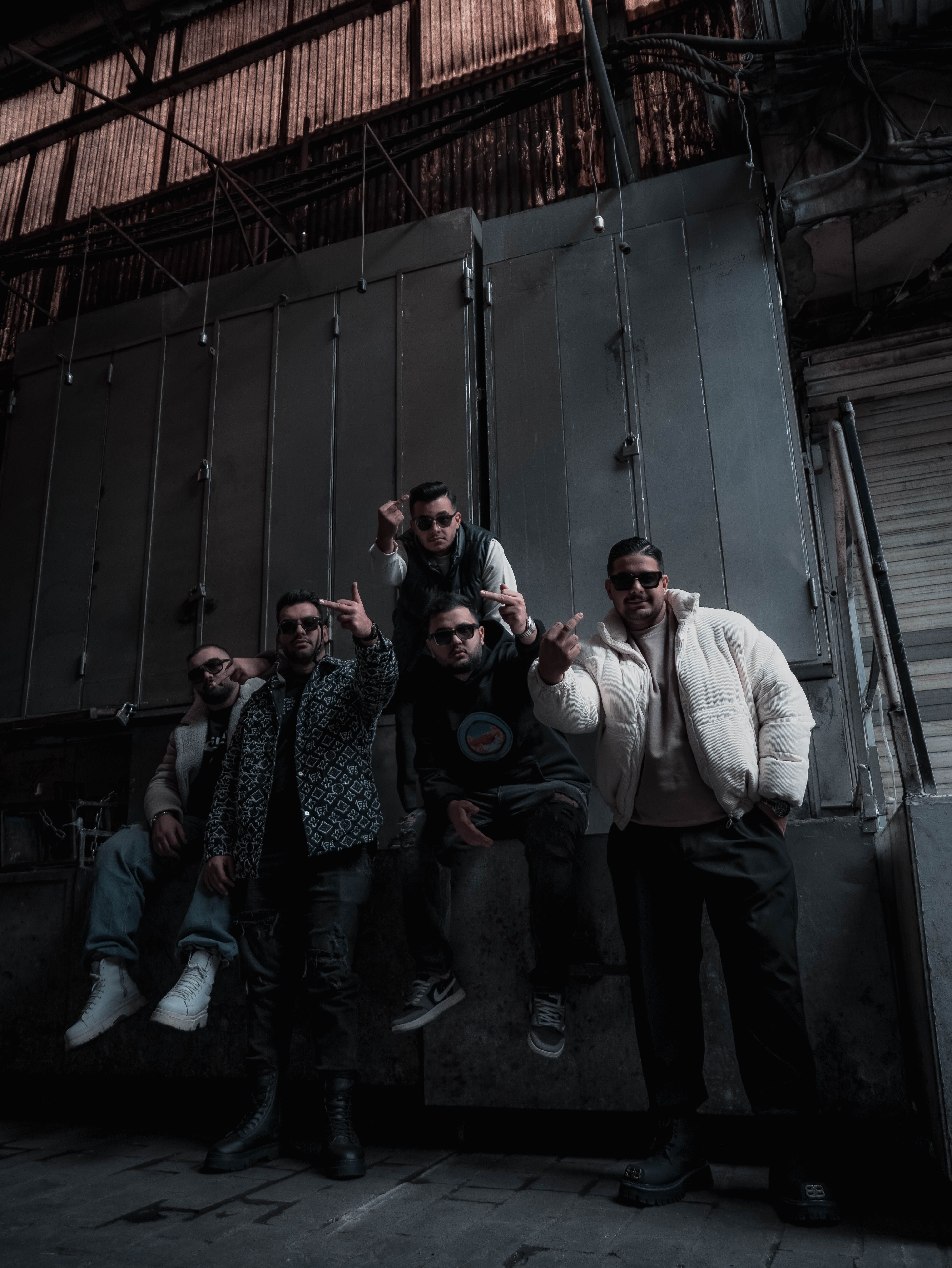Five adults in trendy outfits pose in a dimly lit industrial environment, exuding confidence and style.