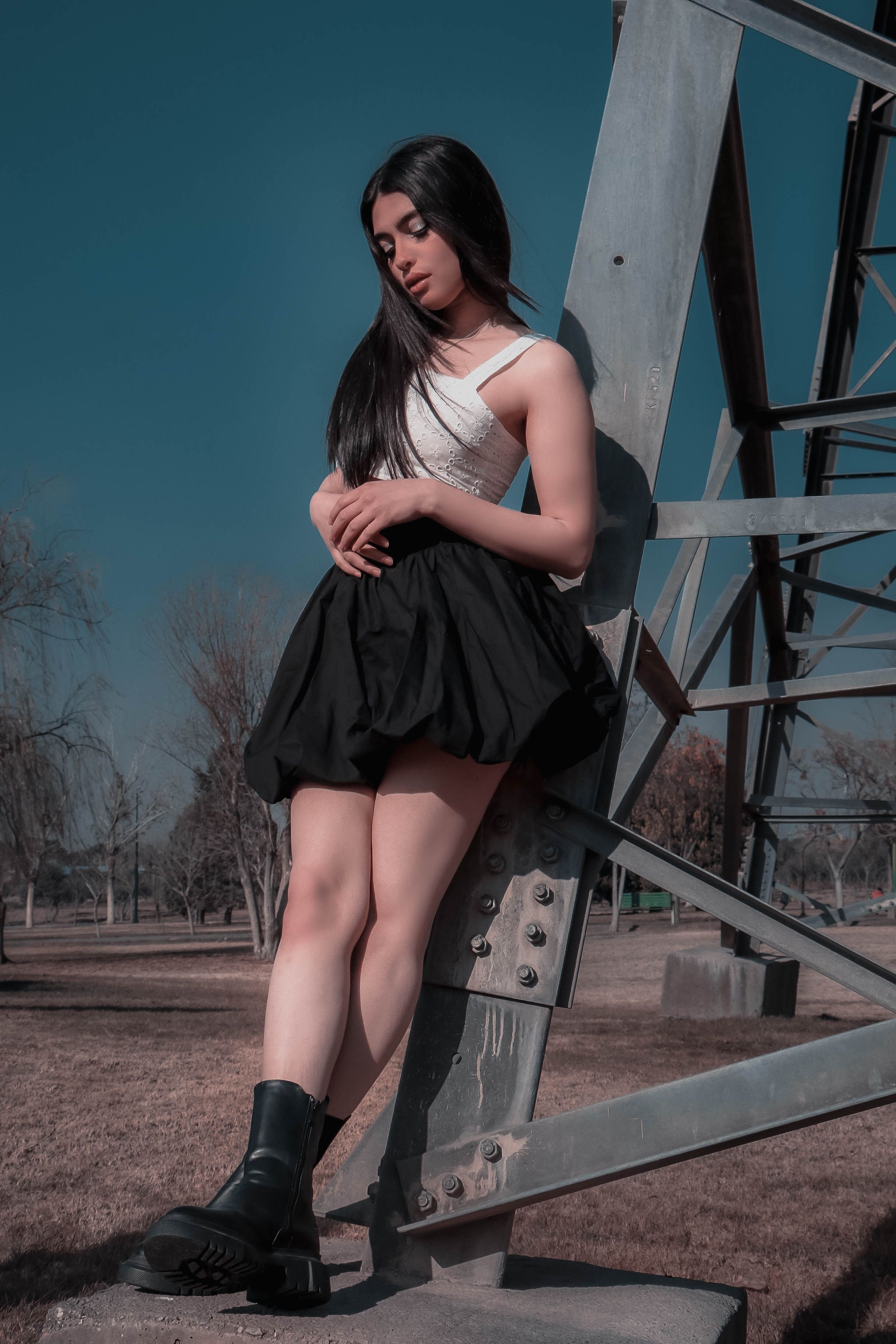 Fashionable woman in black and white outfit posing outside by a metal framework.