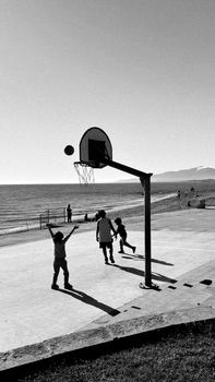 Black and white scene of kids playing basketball near the beach in Cambrils, Spain.