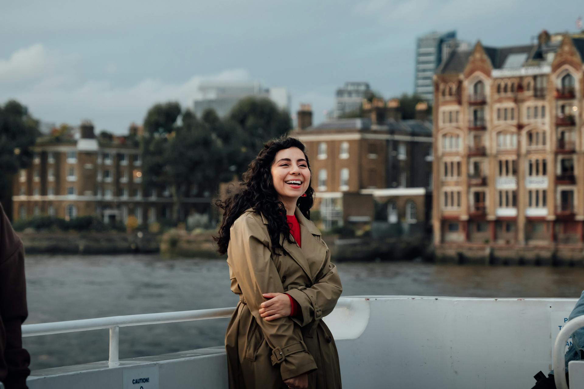 A woman smiles on a ferry with historic London buildings in the background.