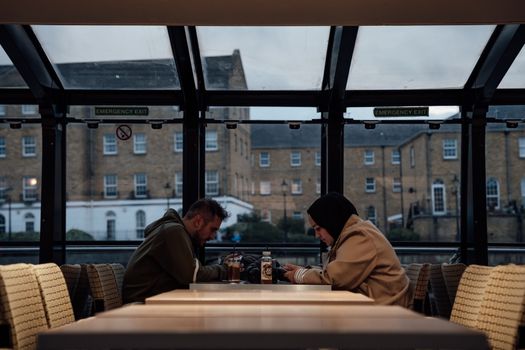 Two adults seated inside a London café with a glass roof, having a casual meal.