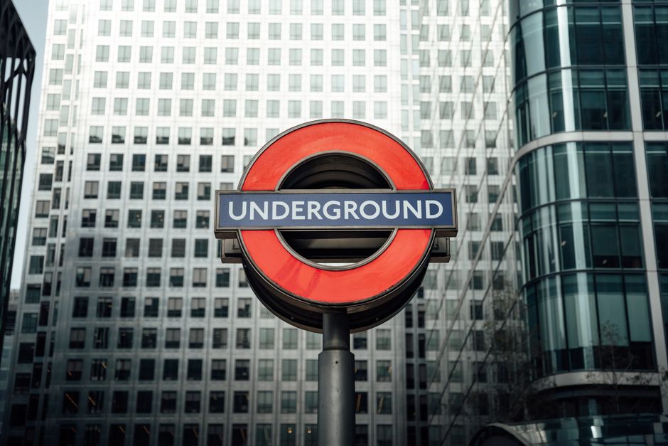 London Underground sign with modern glass buildings in the background, symbolizing urban transportation.