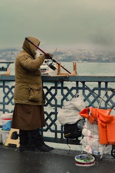 A person fishing on an urban bridge with cityscape background under cloudy sky.