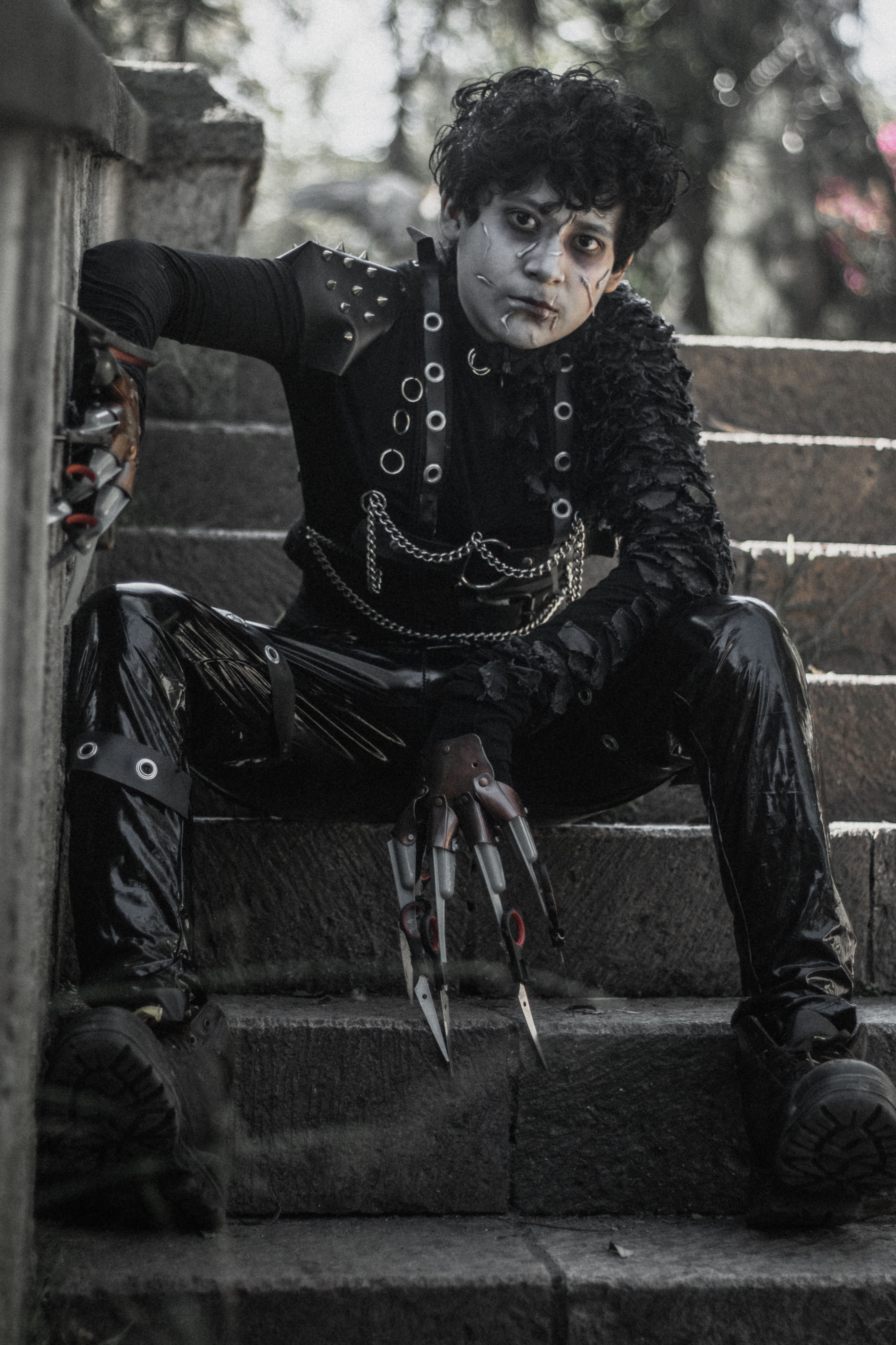 A striking portrait of an individual in gothic costume sitting on stone stairs at a park.