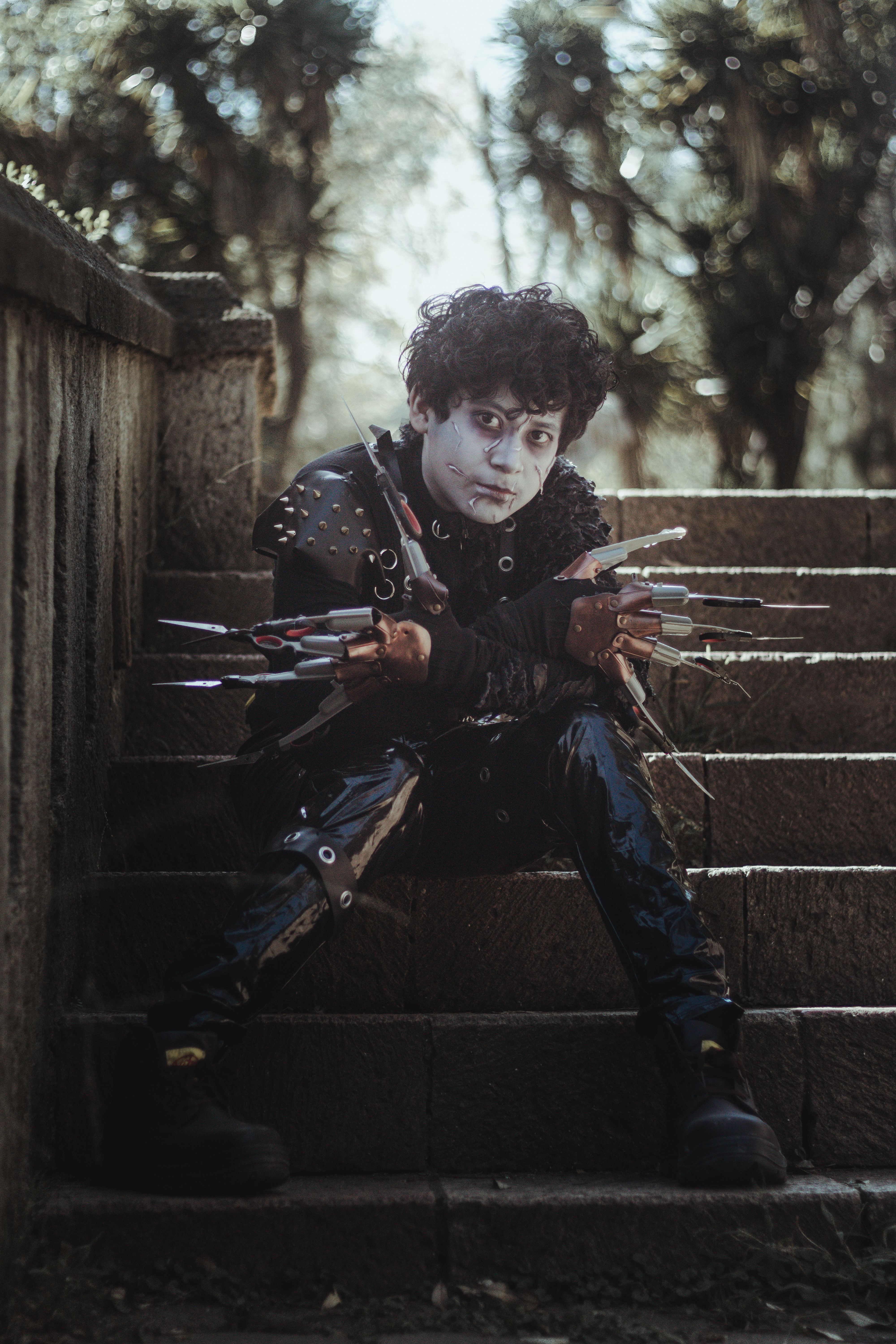 A person in gothic cosplay sits on stone steps under sunlight, showcasing dark fantasy style.