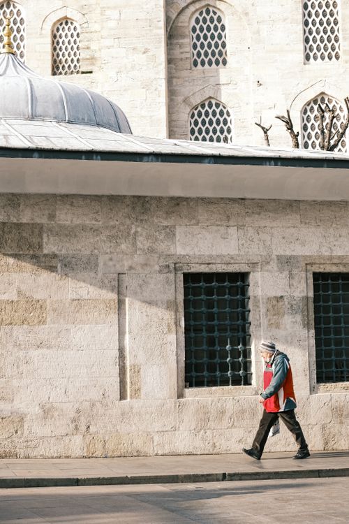 Free An elderly man walks past a historic stone building with arched windows. Bright daylight. Stock Photo