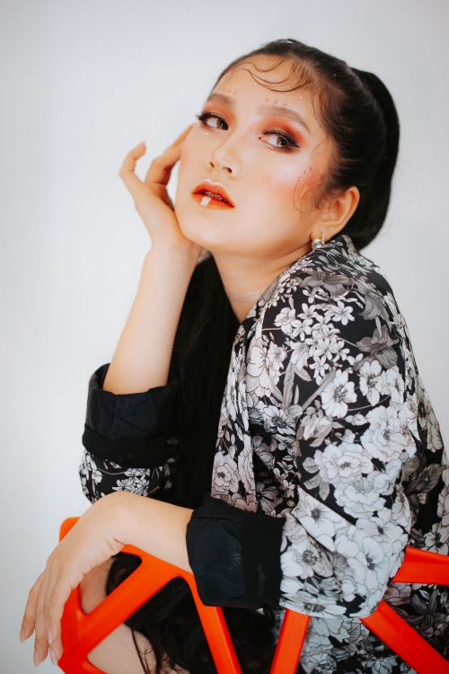 Free A fashionable woman with dramatic makeup and floral outfit poses for a portrait. Stock Photo