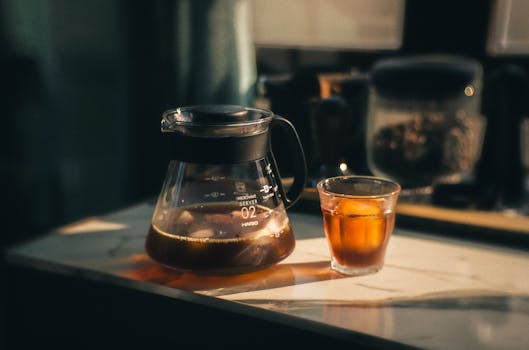 A serene still life of iced coffee in glass and carafe, bathed in warm sunlight on a marble countertop.