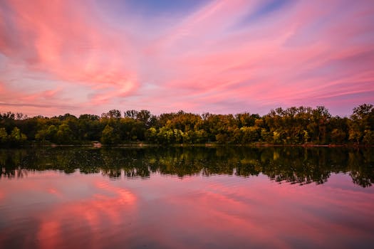 宁静的湖面倒映着令人惊叹的日落，色彩缤纷的云彩与郁郁葱葱的树木相映成趣