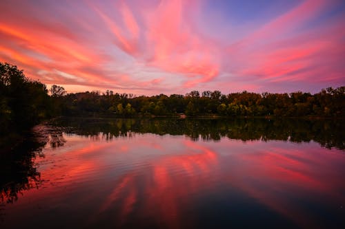 Free Lake Surrounded With Tall and Green Trees Under Orange and Blue Skies Stock Photo