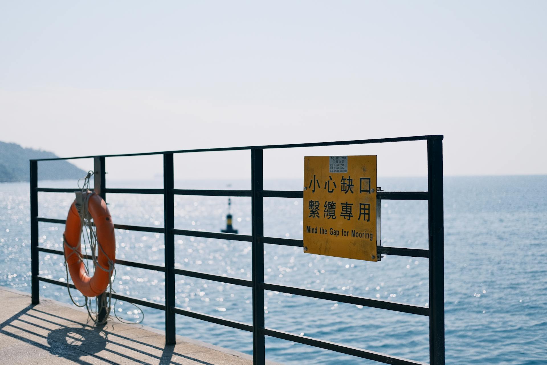 A peaceful seaside dock with a lifebuoy and warning sign on a sunny day.