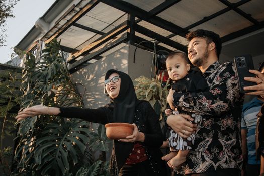 A joyful family moment in a lush Surabaya backyard, capturing cultural traditions. - Fotografer Sidoarjo