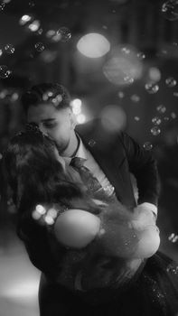A couple shares a romantic dance amidst floating bubbles, captured in a dreamy black and white aesthetic.