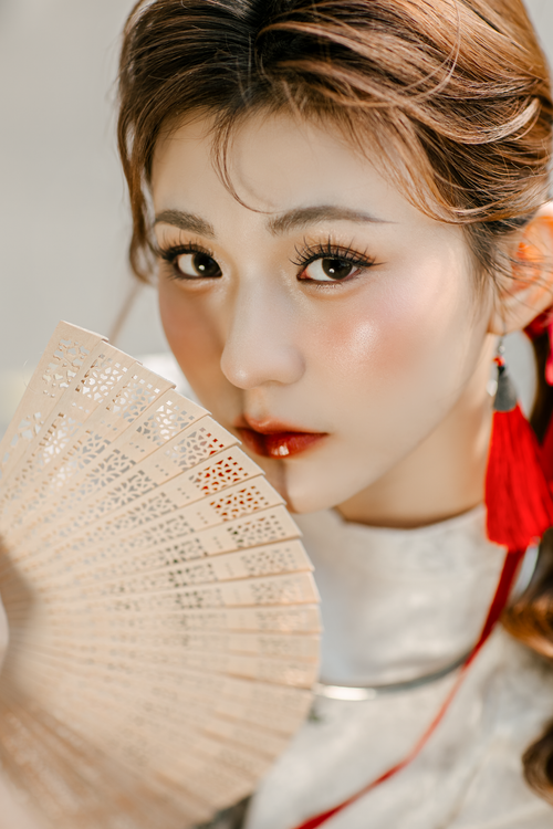 Free Elegant young woman with red earrings holding a decorative fan, showcasing beauty and grace. Stock Photo
