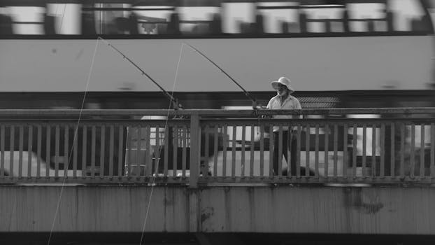 A man fishing on a bridge in Istanbul with motion blur effect in black and white.