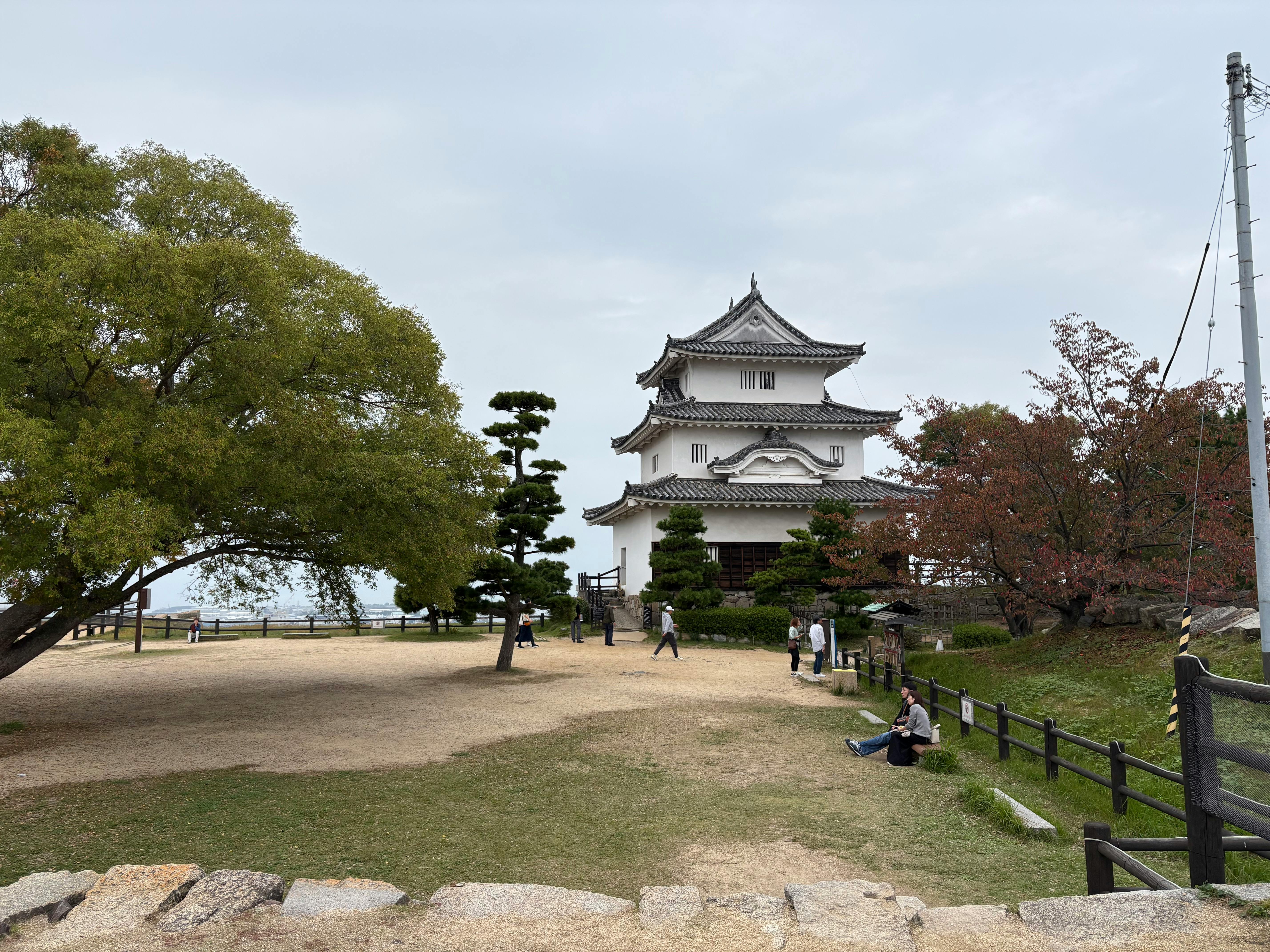 Scenic view of a traditional Japanese castle with lush trees and people enjoying the serene environment.