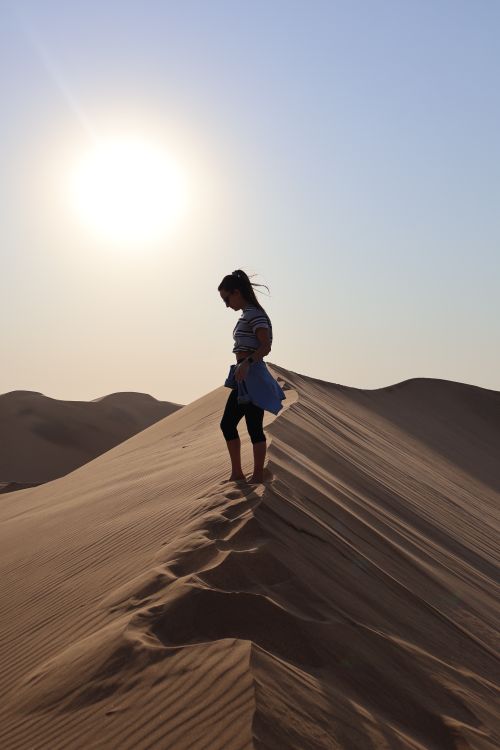 Free A woman stands atop a desert dune, silhouetted against the setting sun. Peaceful and serene. Stock Photo