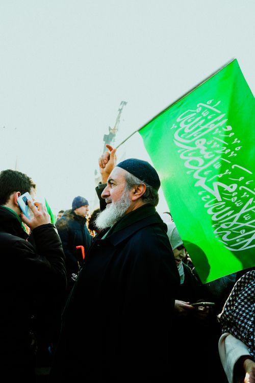 Free Bearded man with flag at public demonstration, holding green banner with Arabic script. Stock Photo