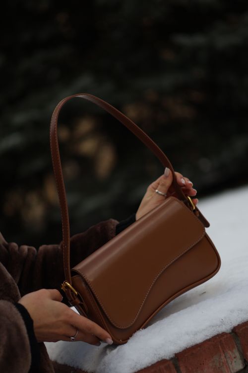 Free Chic brown leather handbag held by a woman outdoors, exuding elegance and style. Stock Photo
