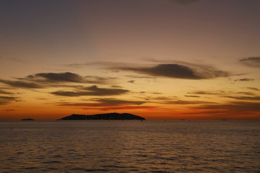 Capture the serene beauty of a summer sunset with warm hues over the calm ocean waters.