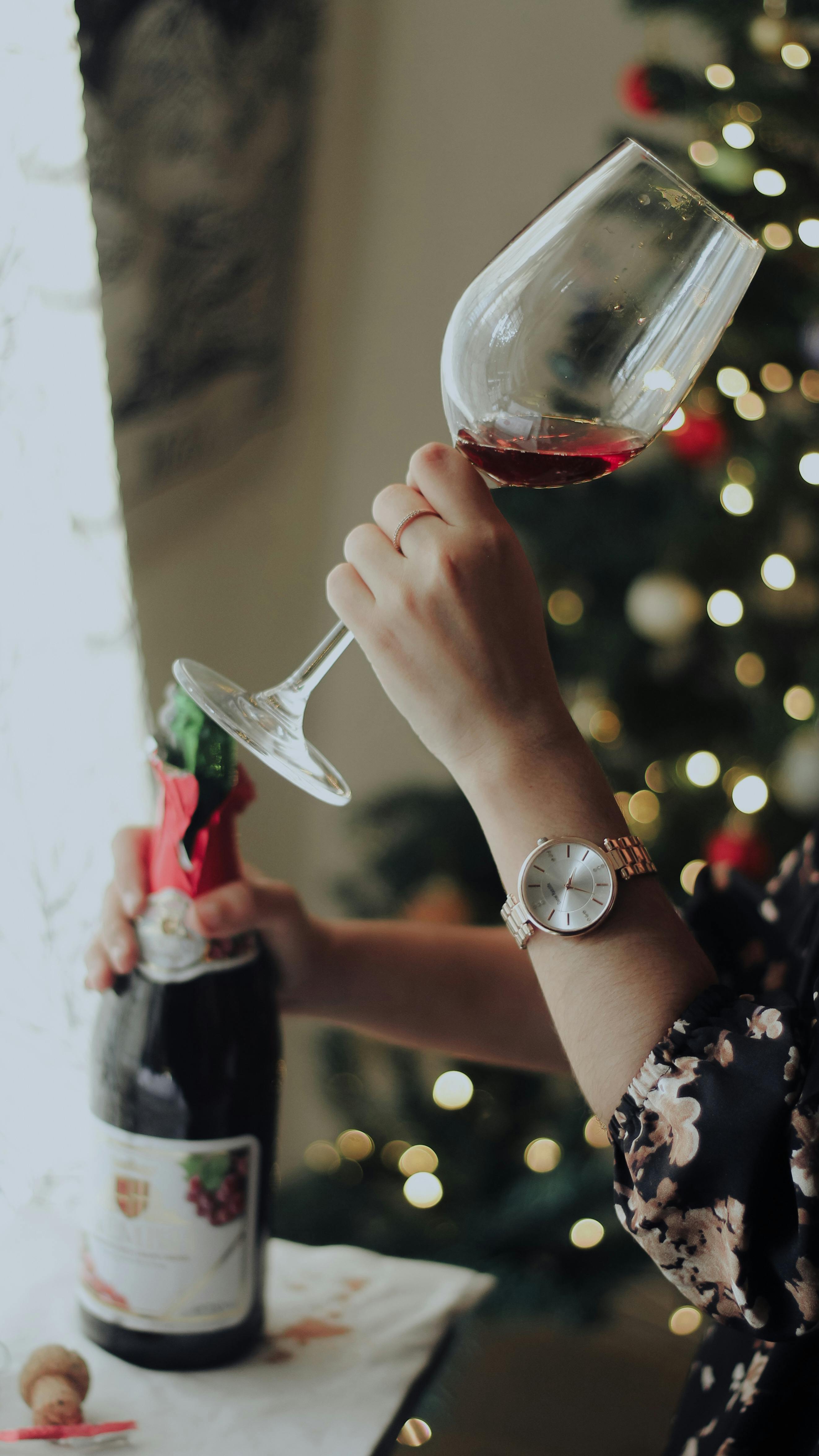 Elegant hand holding a glass of red wine, with a festive Christmas background.