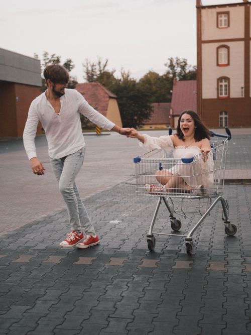 Free Couple having fun with a shopping cart outdoors, capturing youthful joy and playfulness. Stock Photo