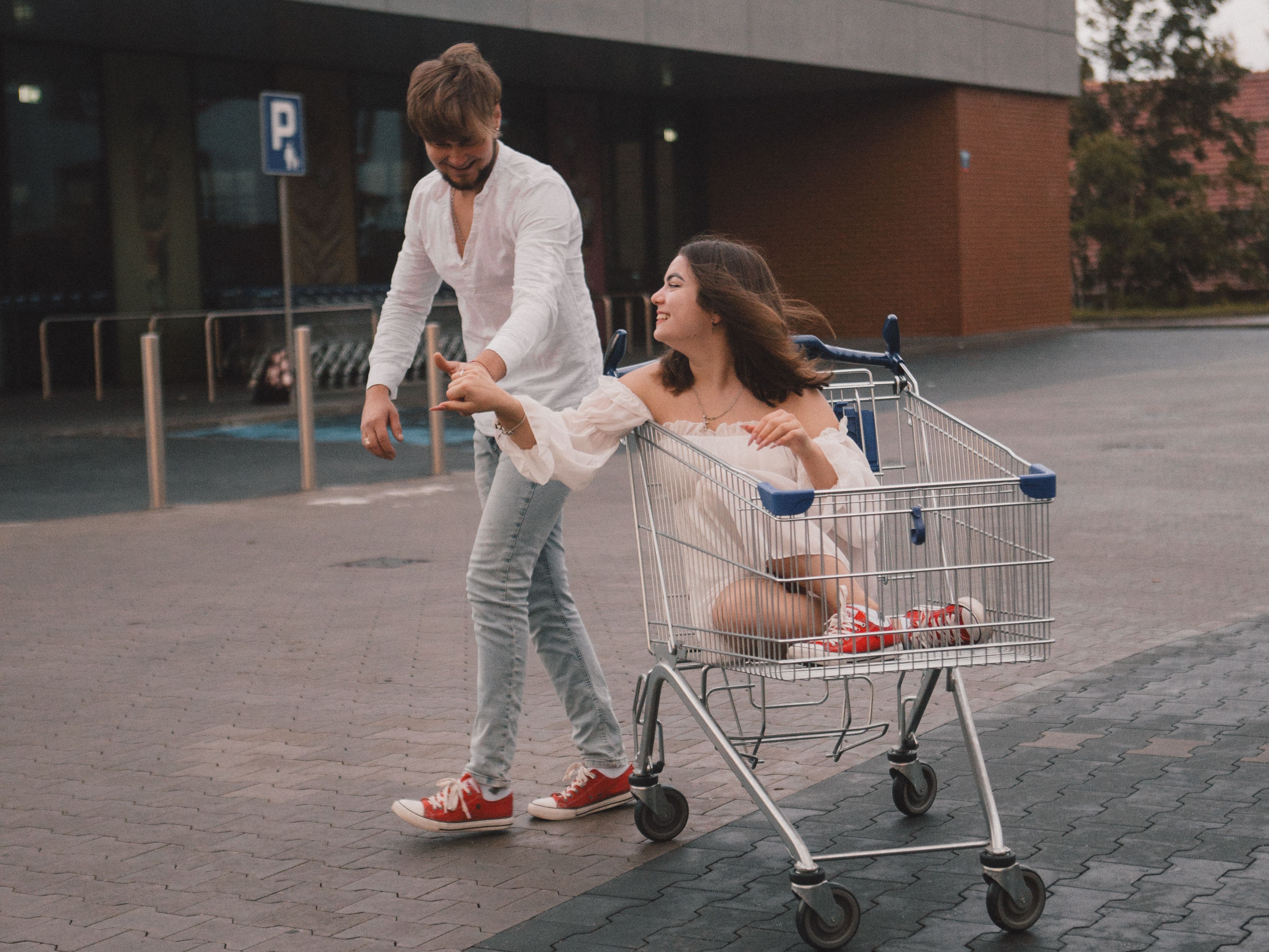 A joyful couple enjoying a playful moment with a shopping cart outdoors.