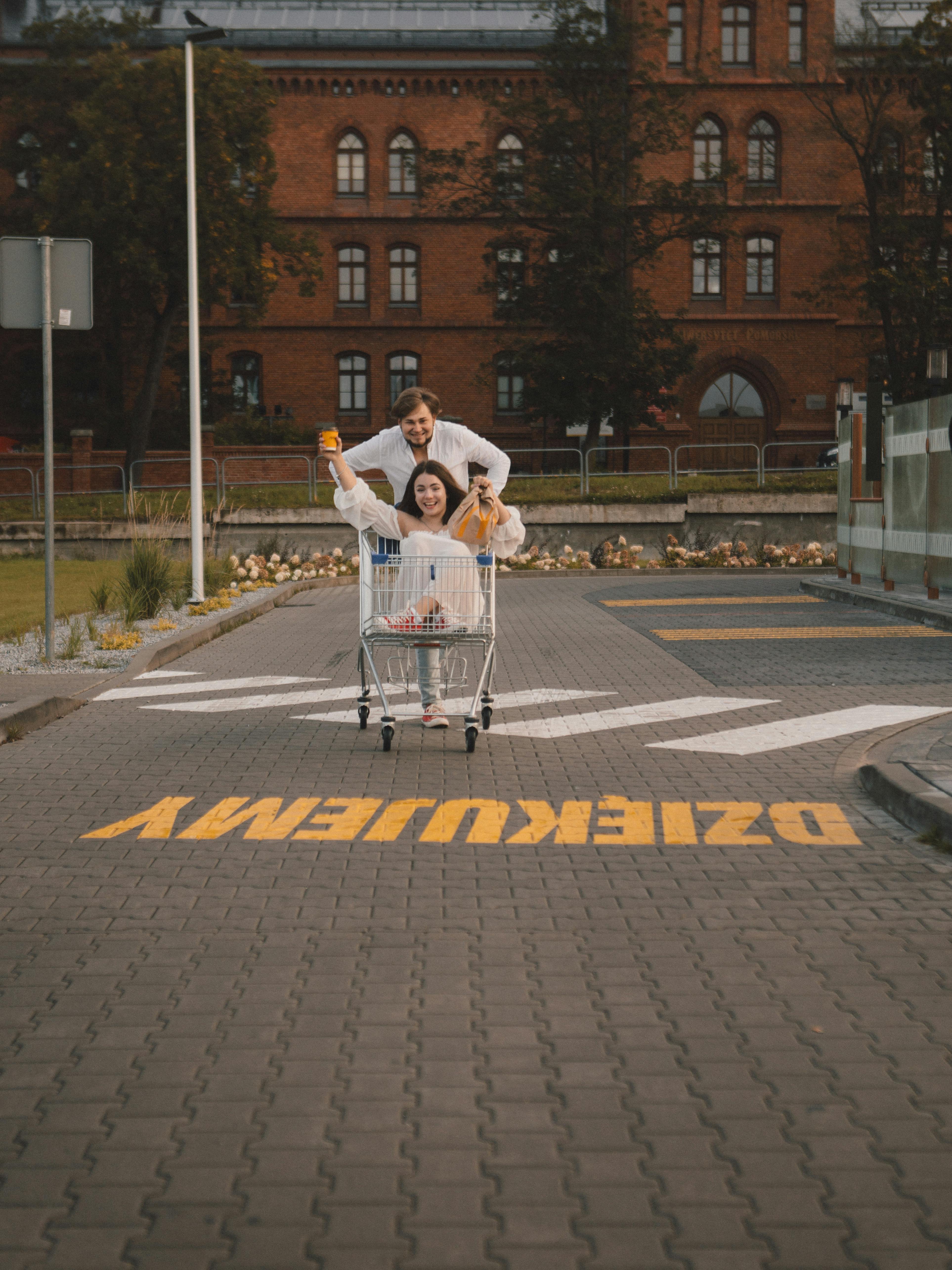 Two friends having fun with a shopping cart on an urban street, enjoying the moment.
