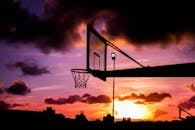令人惊叹的篮球篮轮廓与鲜艳的日落天空相映衬，云层引人注目