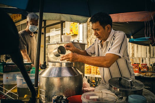 Street vendor skillfully prepares authentic Asian food in bustling market scene.