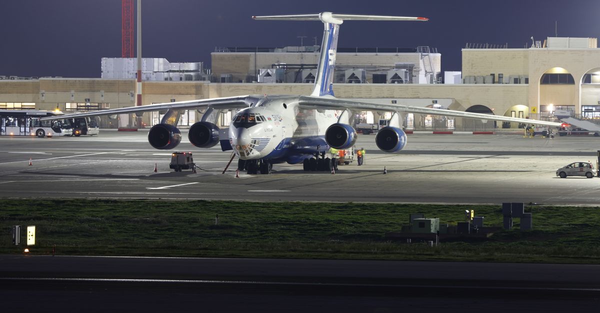 A large cargo aircraft parked on an airport runway at night, under bright lights.