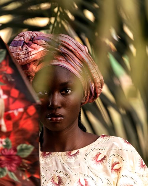 Free Elegant portrait of a woman in colorful headwrap surrounded by foliage. Stock Photo