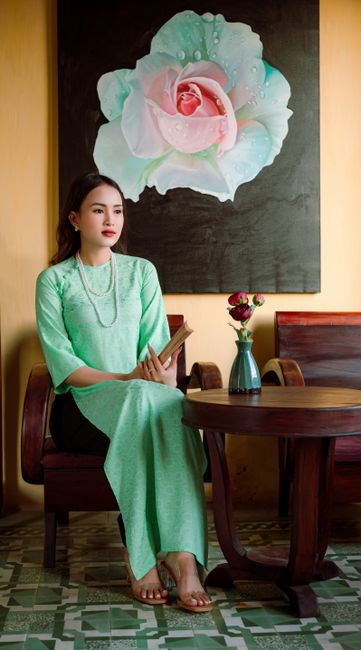 Portrait of a Vietnamese woman in a green ao dai seated indoors, showcasing cultural heritage.