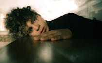 一位年轻人躺在室内，特写肖像展示了他独特的卷发和深思的表情