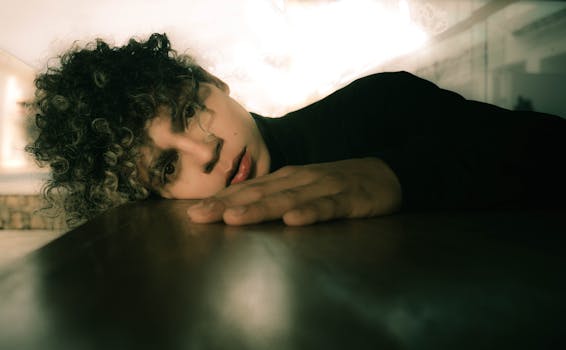 一位年轻人躺在室内，特写肖像展示了他独特的卷发和深思的表情