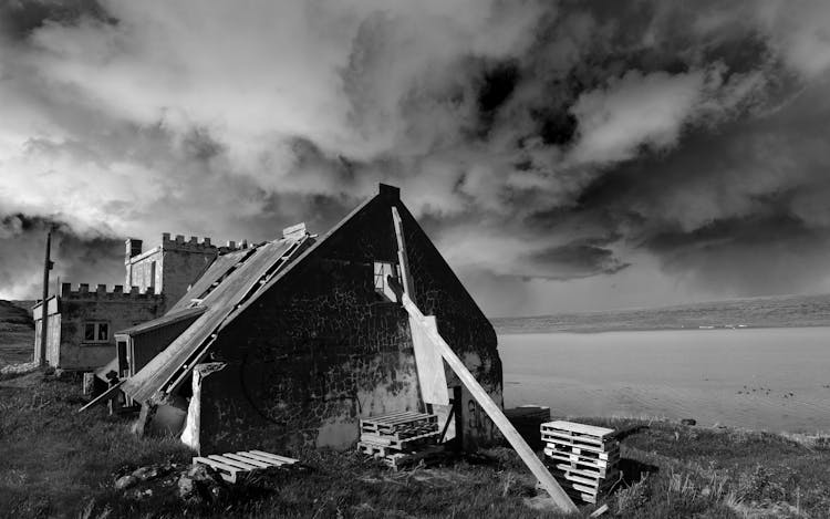 Grayscale Photo Of House Under Cloudy Sky