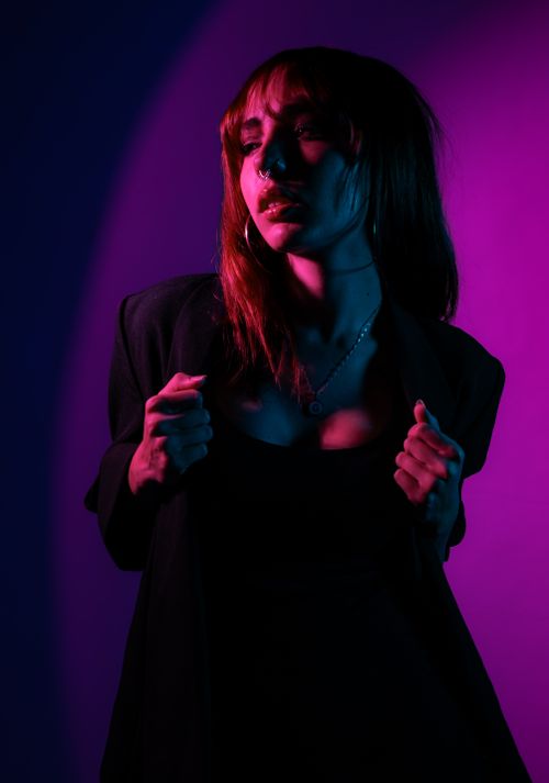 Free Artistic portrait of a woman in dramatic pink and blue lighting with a bold fashion pose. Stock Photo