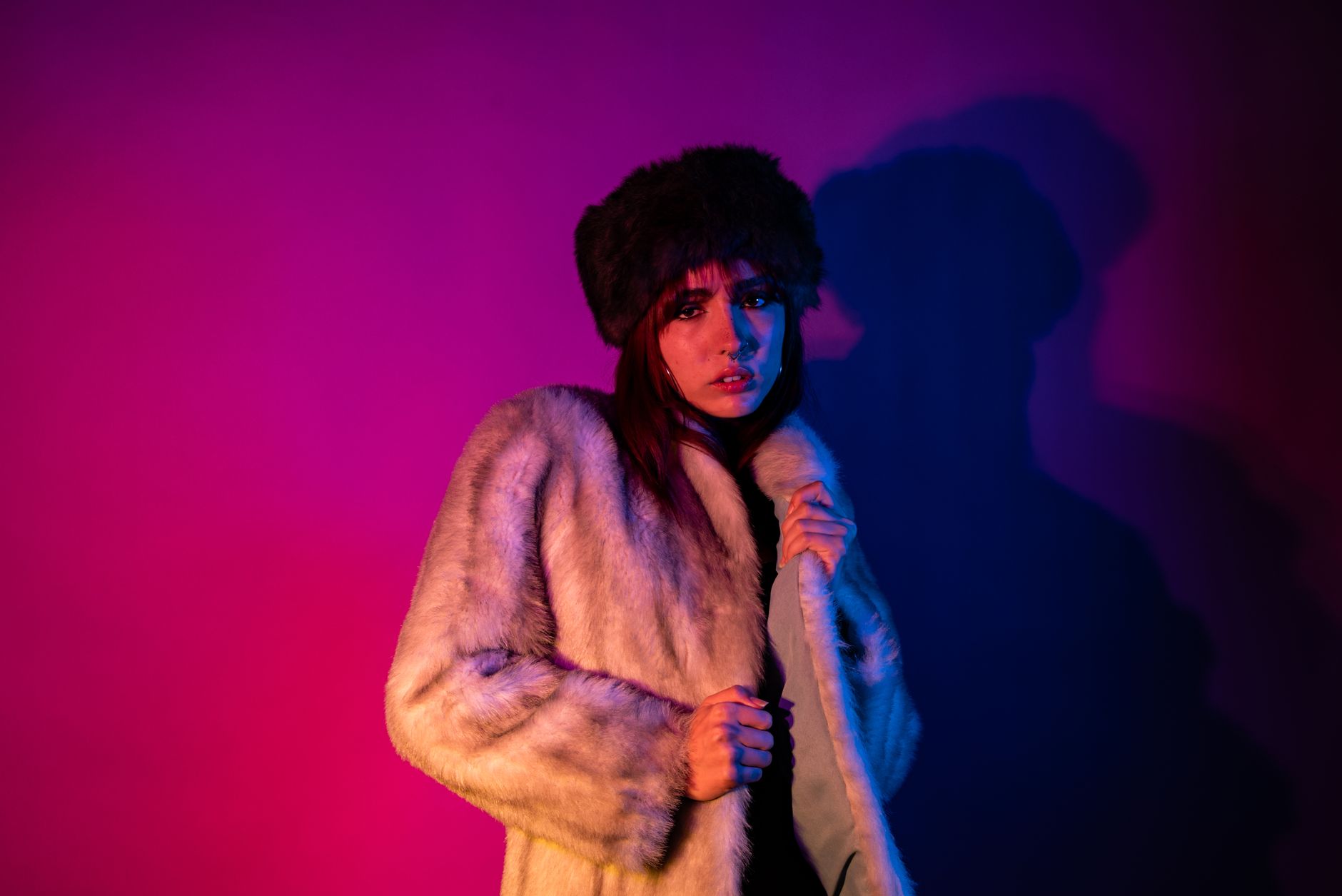 Fashionable woman in a luxurious fur coat, standing in vibrant neon blue and pink light.