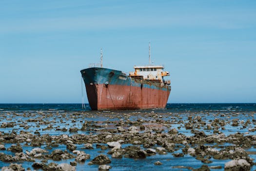 Abandoned rusty ship resting on a rocky shoreline against a clear blue sky.