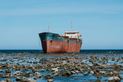 Free Abandoned rusty ship resting on a rocky shoreline against a clear blue sky. Stock Photo