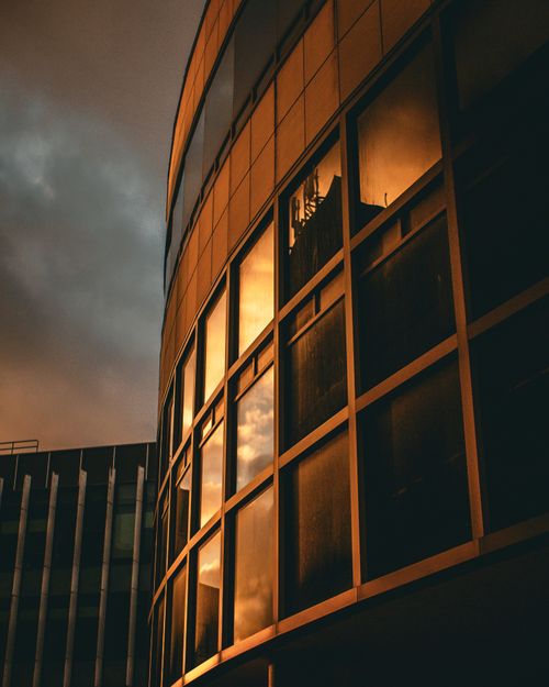 Free A modern building reflecting a dramatic sunset sky with warm tones. Stock Photo