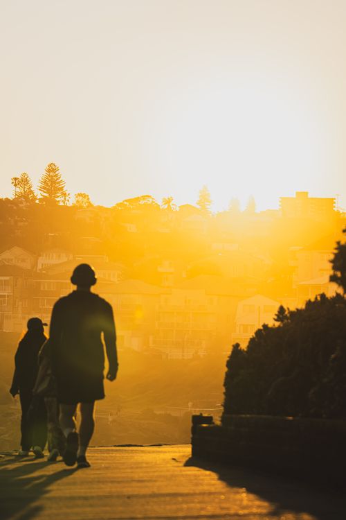 Free Silhouetted figures walk along a scenic path during a vibrant sunrise with a warm glow. Stock Photo