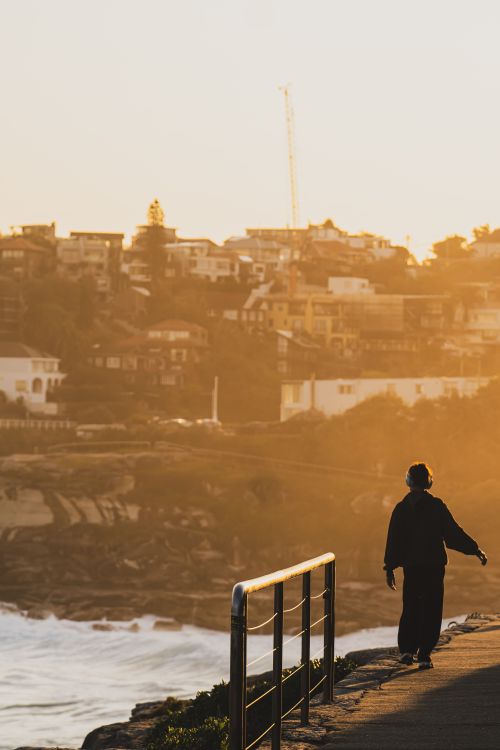 Free A solitary figure walks along a coastal path at sunset, overlooking seaside houses. Stock Photo