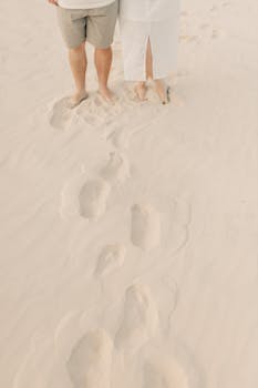 A couple's feet and footprints on a serene sandy beach.