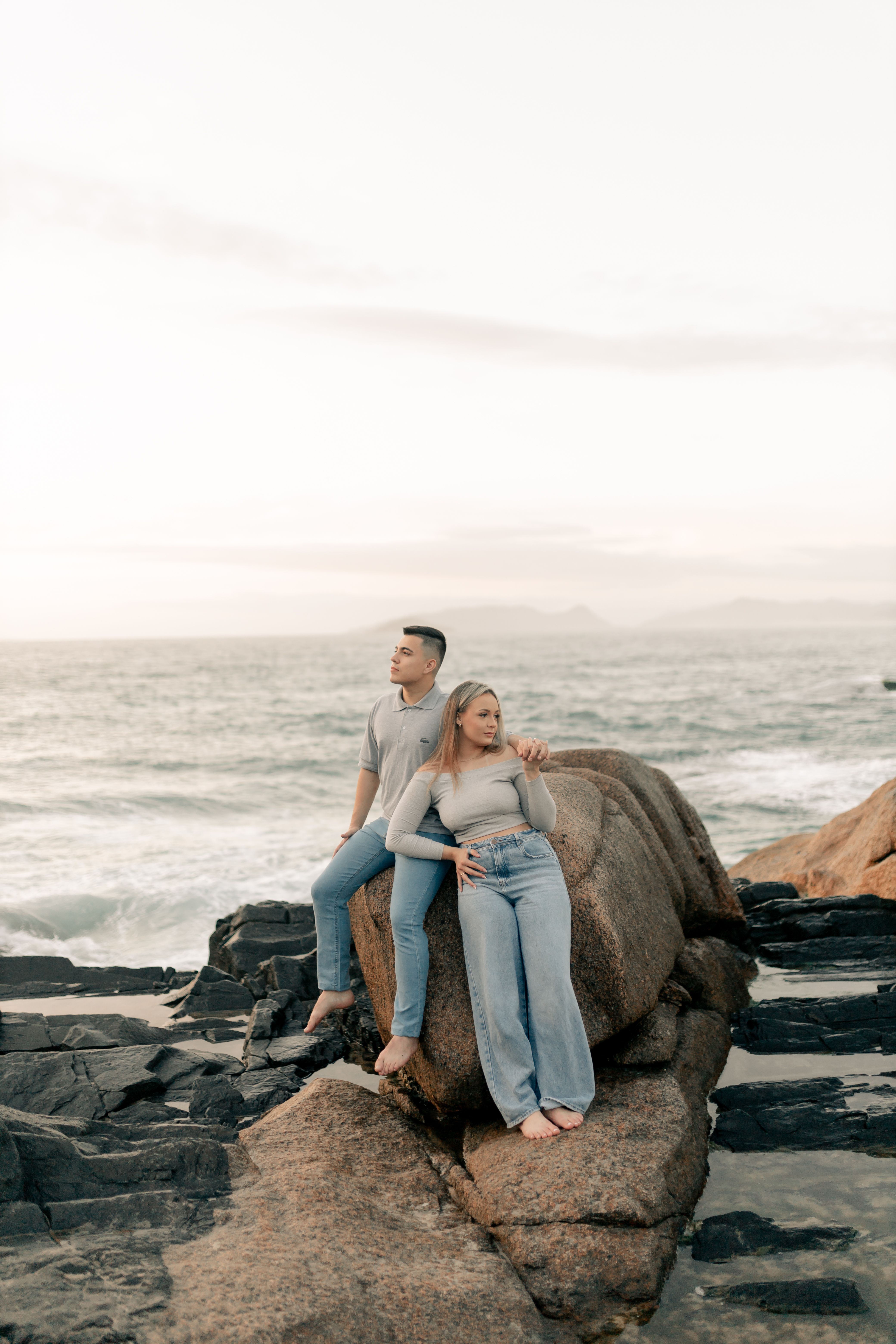 A couple sitting on rocks by the ocean, enjoying a serene sunset. Perfect romantic getaway setting.