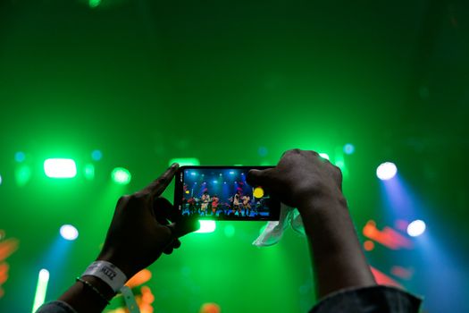 A vibrant live concert scene captured through a smartphone under green stage lighting.
