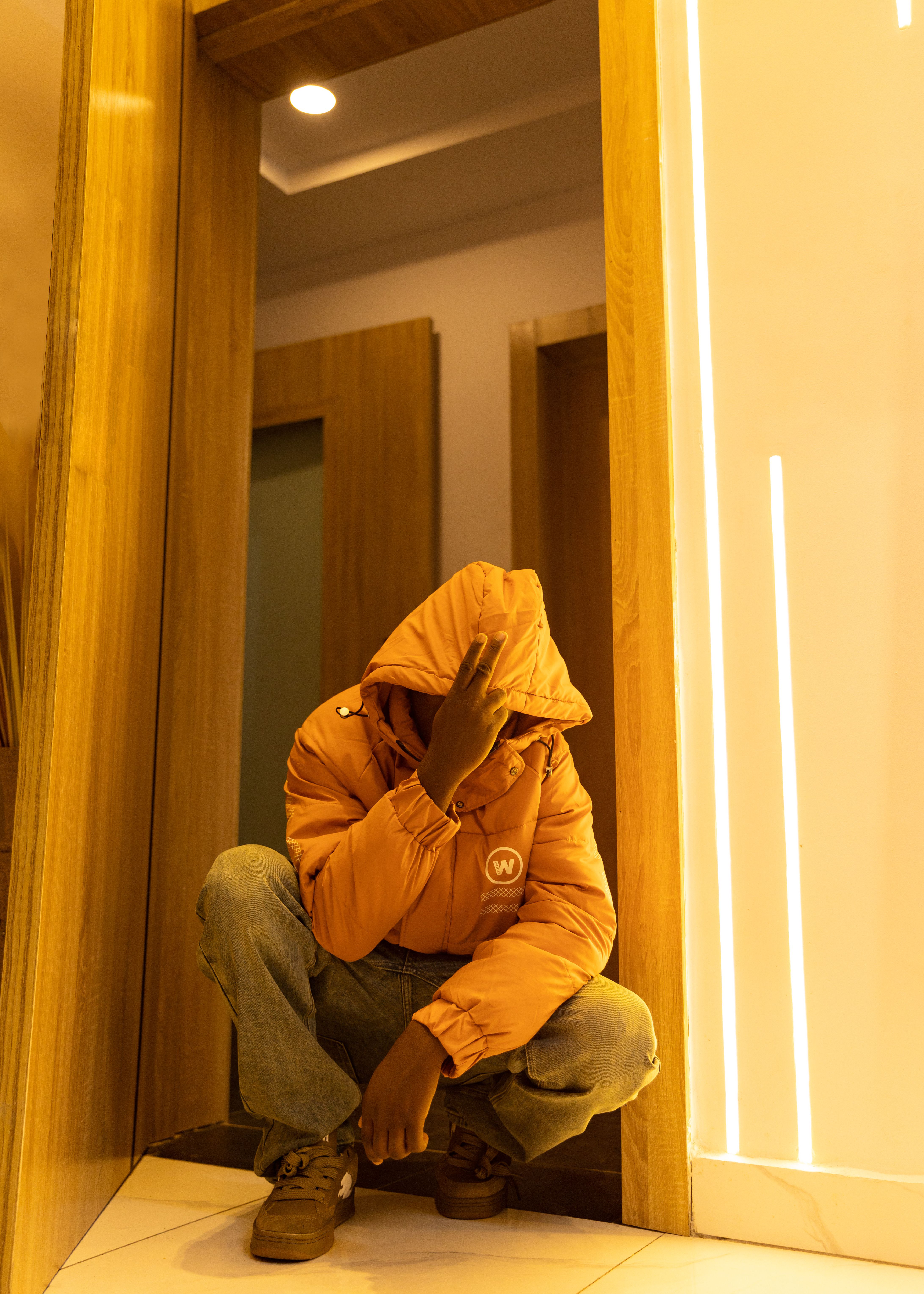 Urban streetwear style with an orange jacket, posing indoors.