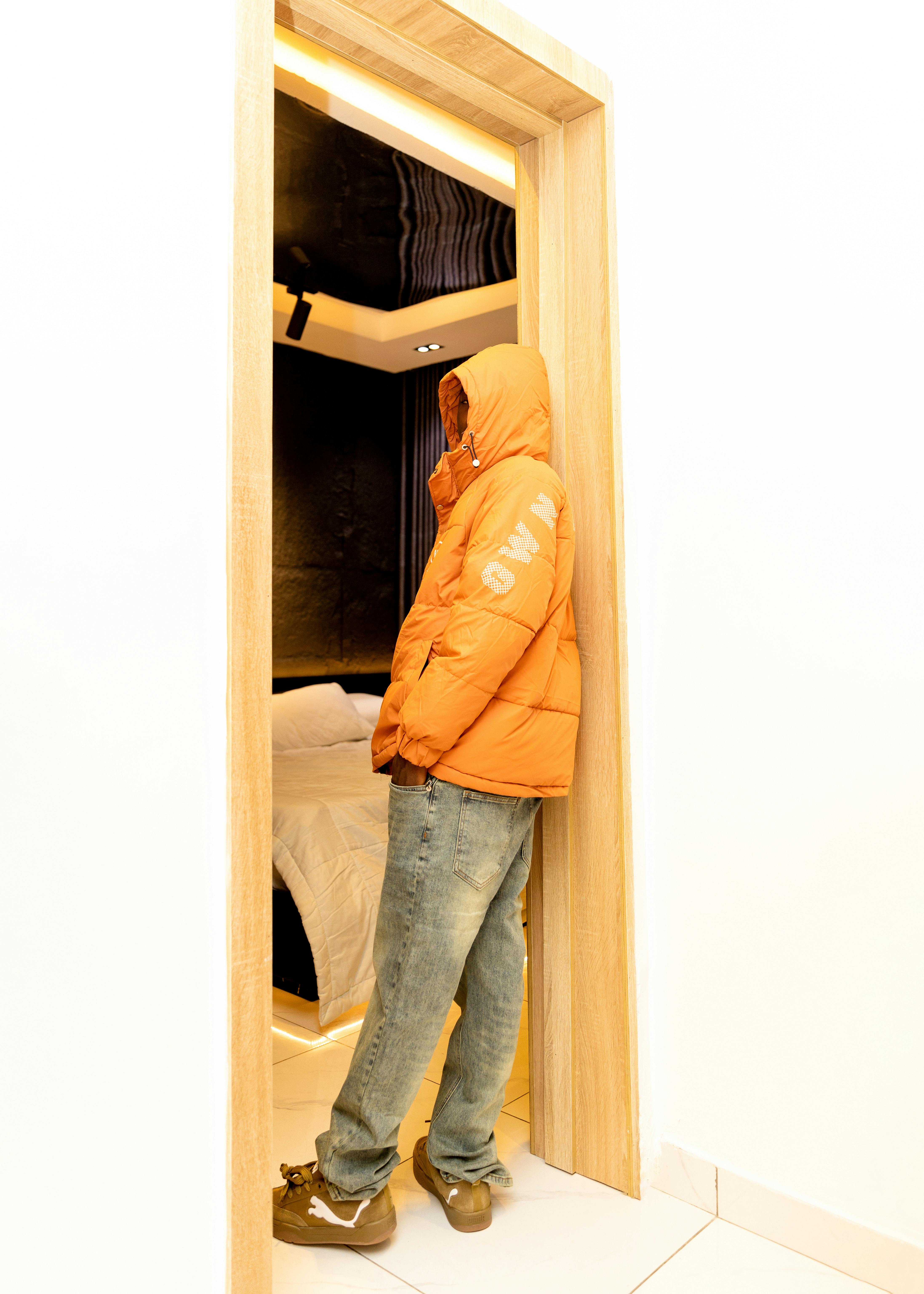 Person in an orange jacket stands in a doorway, highlighting casual indoor fashion.